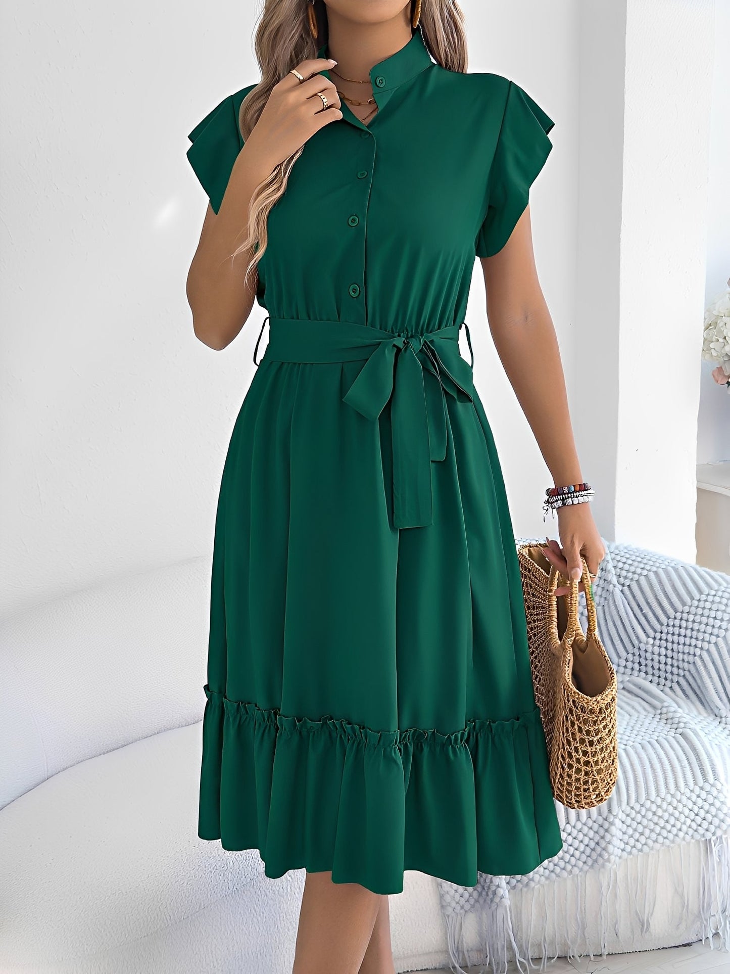 Green - A woman wearing a woven short-sleeve midi shirt dress with a collared neckline, button-down front, tie waist, and tiered ruffle hem, holding a woven bag.