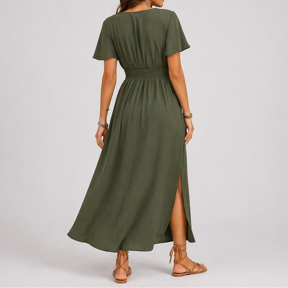 Olive green - A woman modelling a woven V-neck maxi dress featuring short flutter sleeves, a shirred waistline, and a side split, styled with sandals and a woven handbag.