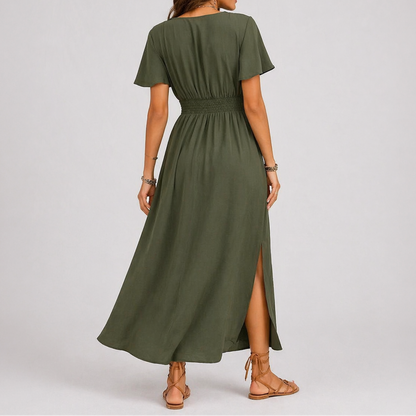 Olive green - A woman modelling a woven V-neck maxi dress featuring short flutter sleeves, a shirred waistline, and a side split, styled with sandals and a woven handbag.